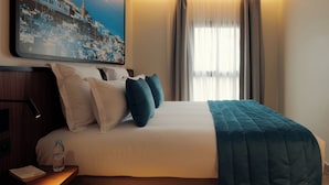 A hotel room with a bed, a nightstand, a water bottle, a framed picture, and a window with curtains. - Mia Hotels Agadir (Agadir)