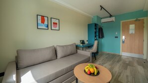 A modern living room with a sofa, a small round table with fruit, a desk with a chair, and an air conditioning unit. - Mia Hotels Agadir (Agadir)