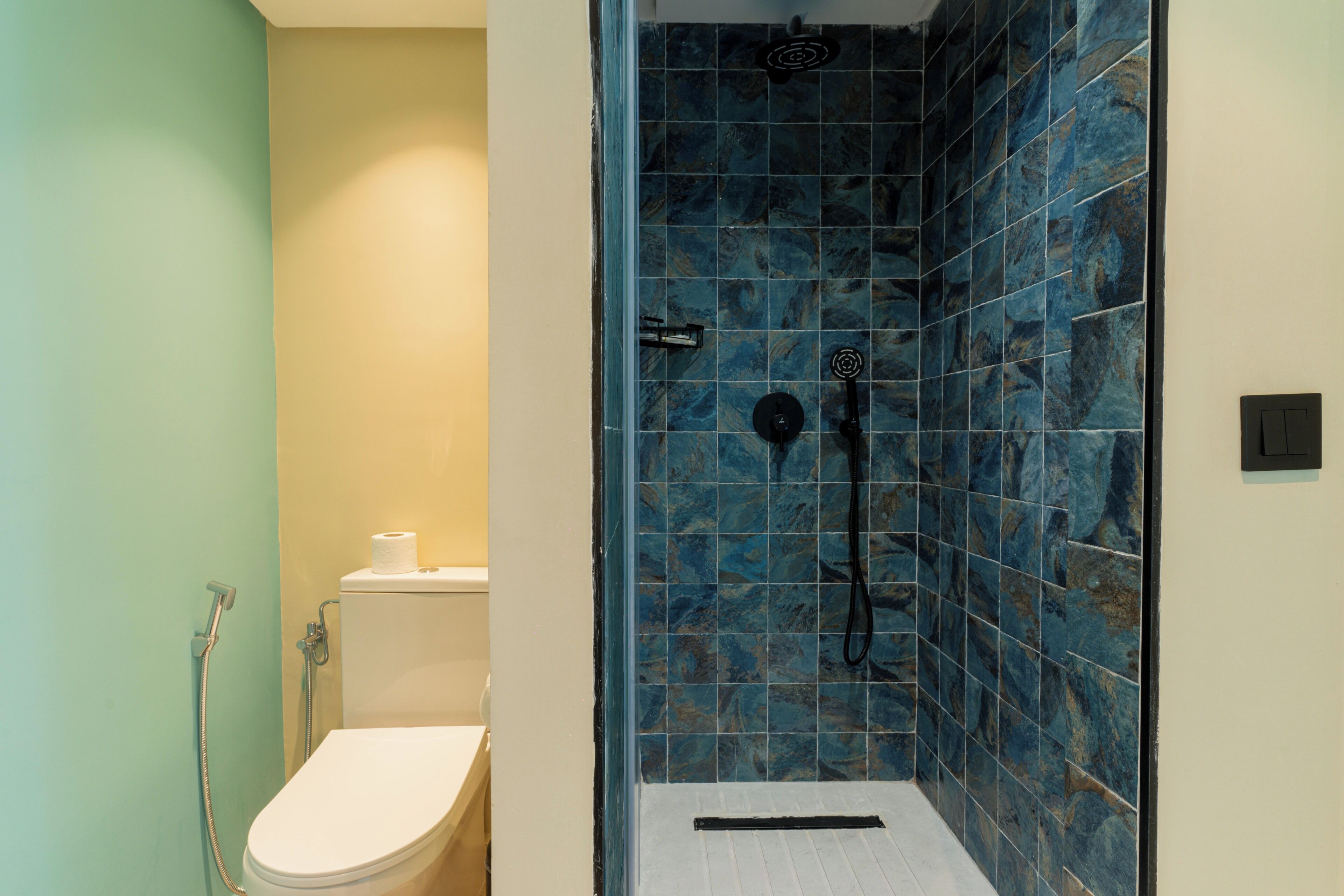A bathroom with a shower, toilet, and a tiled wall.