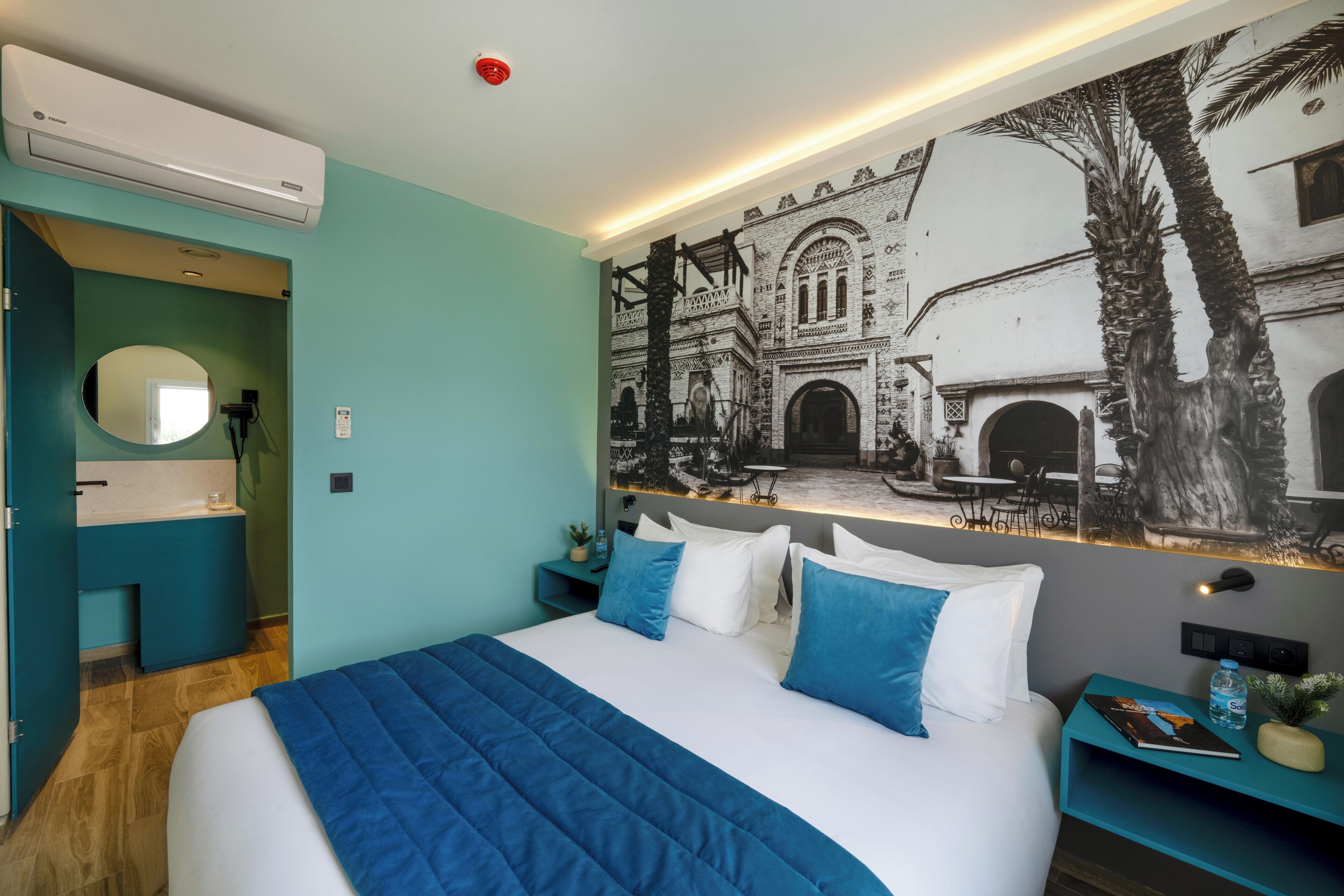 A modern hotel room with a large bed, teal walls, and a mural of a historical building.
