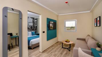 A modern hotel room with a bed, a desk, a sofa, and a small table with fruit.