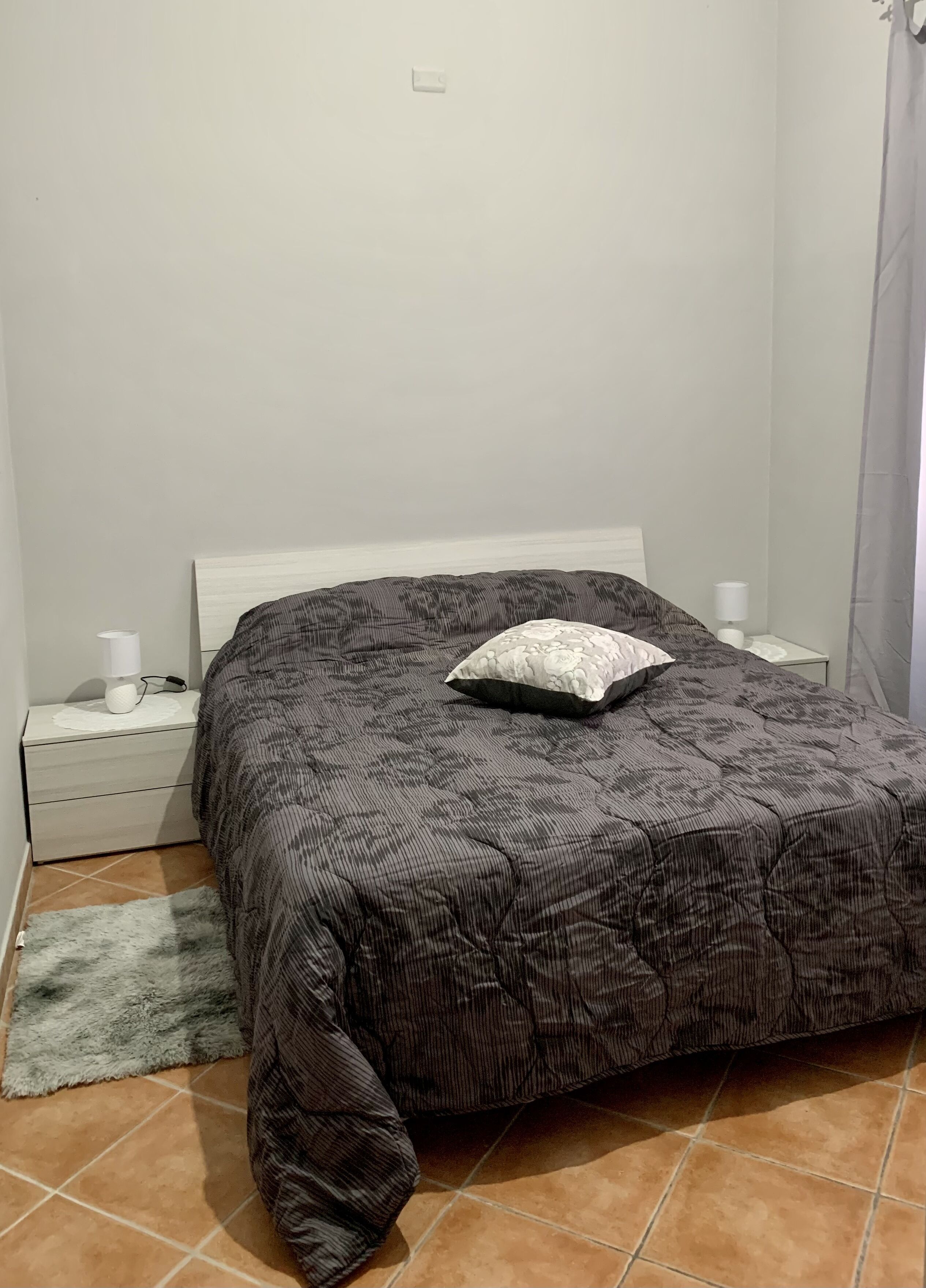 A bedroom with a bed, a nightstand, a lamp, and a rug.