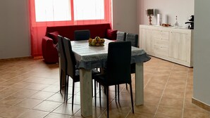 Een eetgedeelte met een tafel voor vier personen, een rode bank en een keuken met kasten en apparatuur.