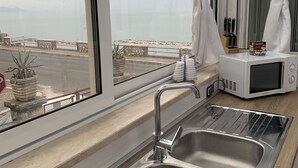 Een moderne keuken met een RVS spoelbak, een magnetron en uitzicht op zee door grote ramen.