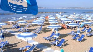 Een strand met talloze blauwe en witte parasols en ligbedden, een heldere lucht en een vlag met het jaartal 2025.