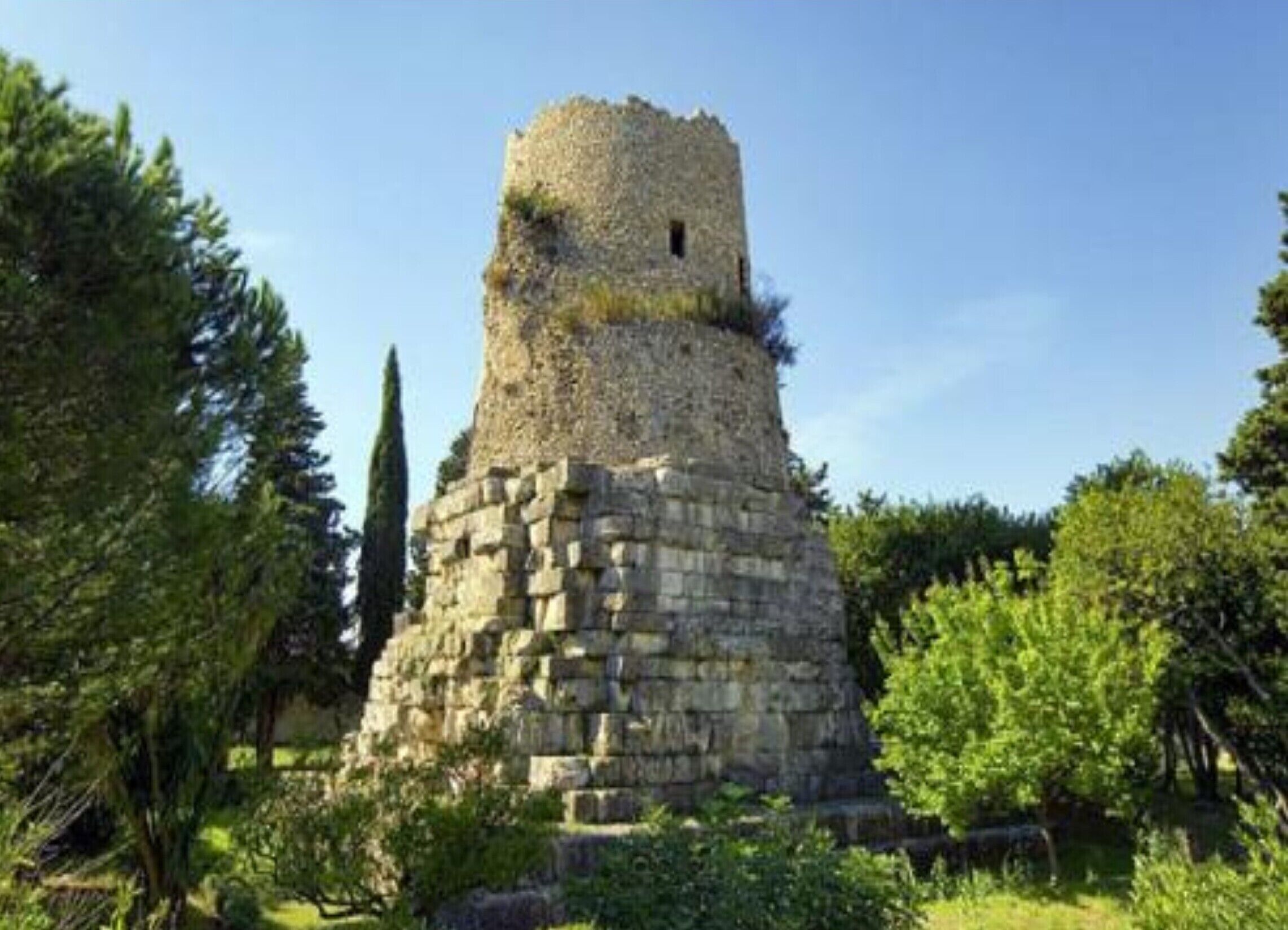 Una torre de piedra con un pequeño ventanal, rodeada de vegetación.