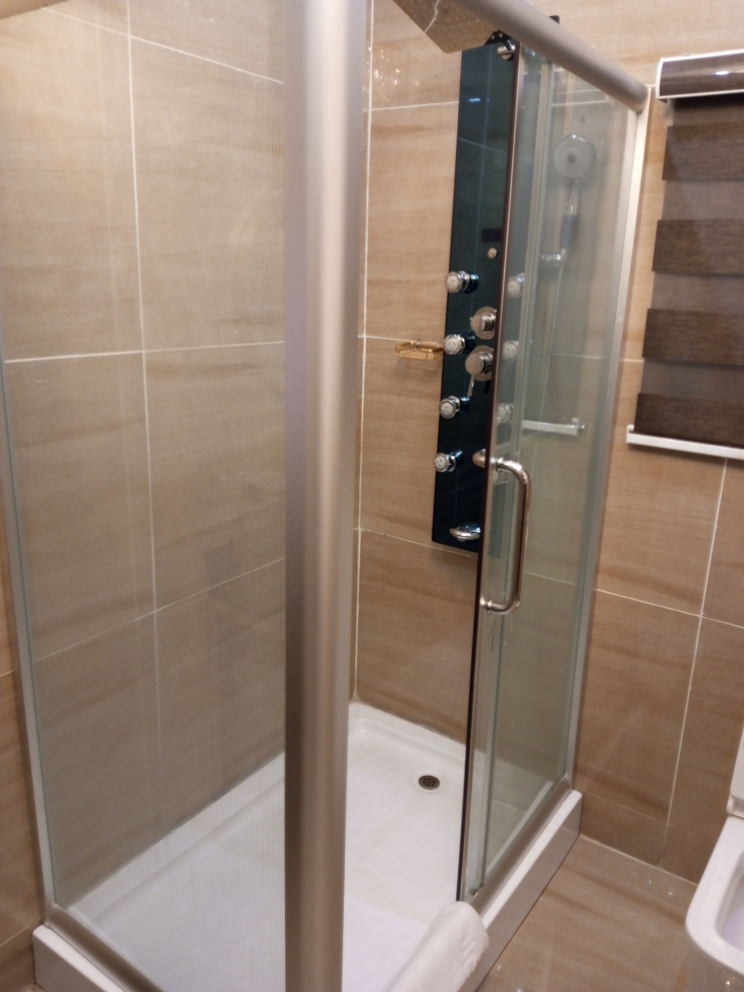 A glass-enclosed shower stall with a stainless steel door, beige tiled walls, and a white floor.