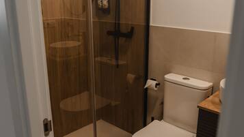 Een moderne badkamer met een douchecabine van glas, een toilet en een houten wastafelmeubel.