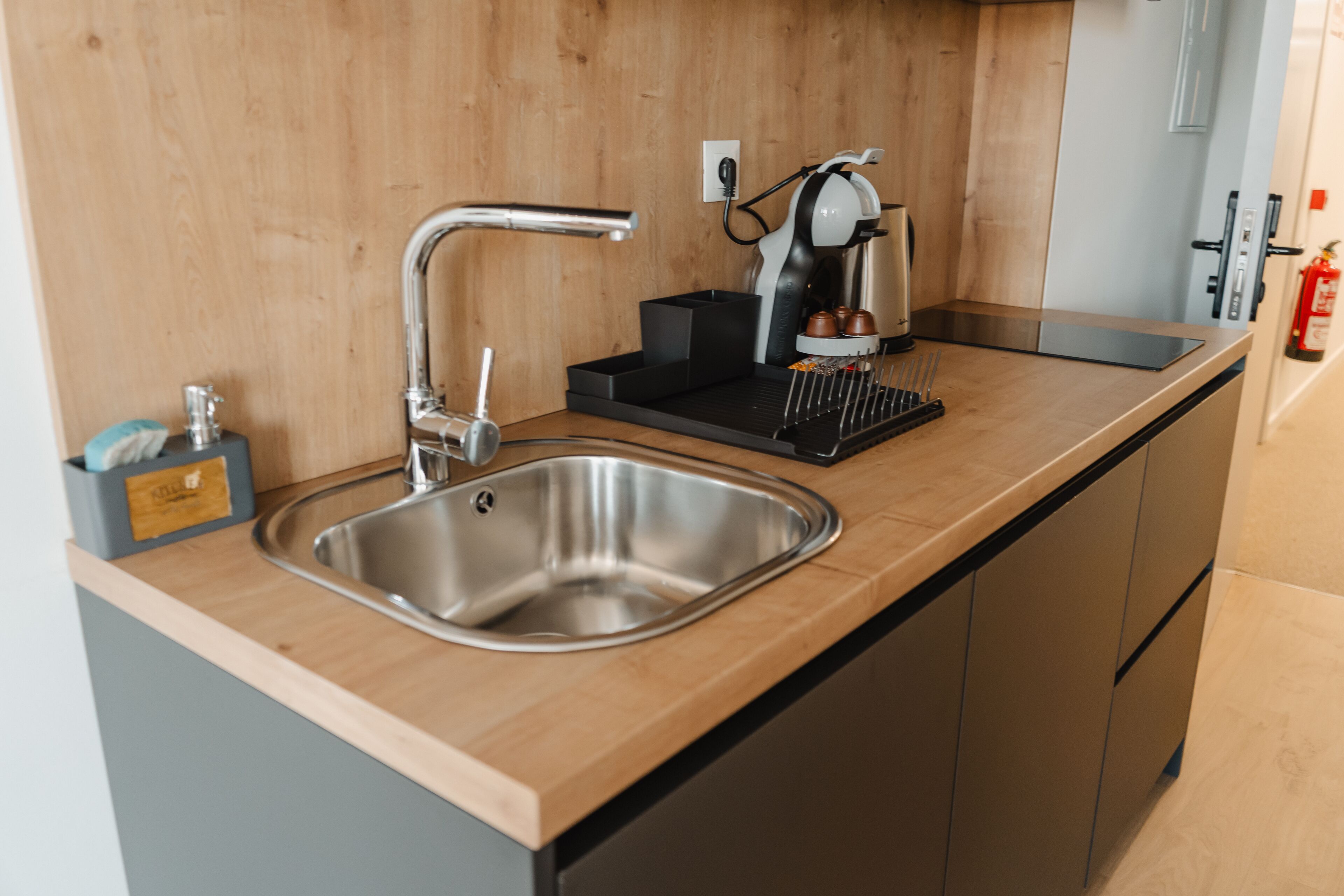 A modern kitchen with a stainless steel sink, a coffee machine, and a black tray.