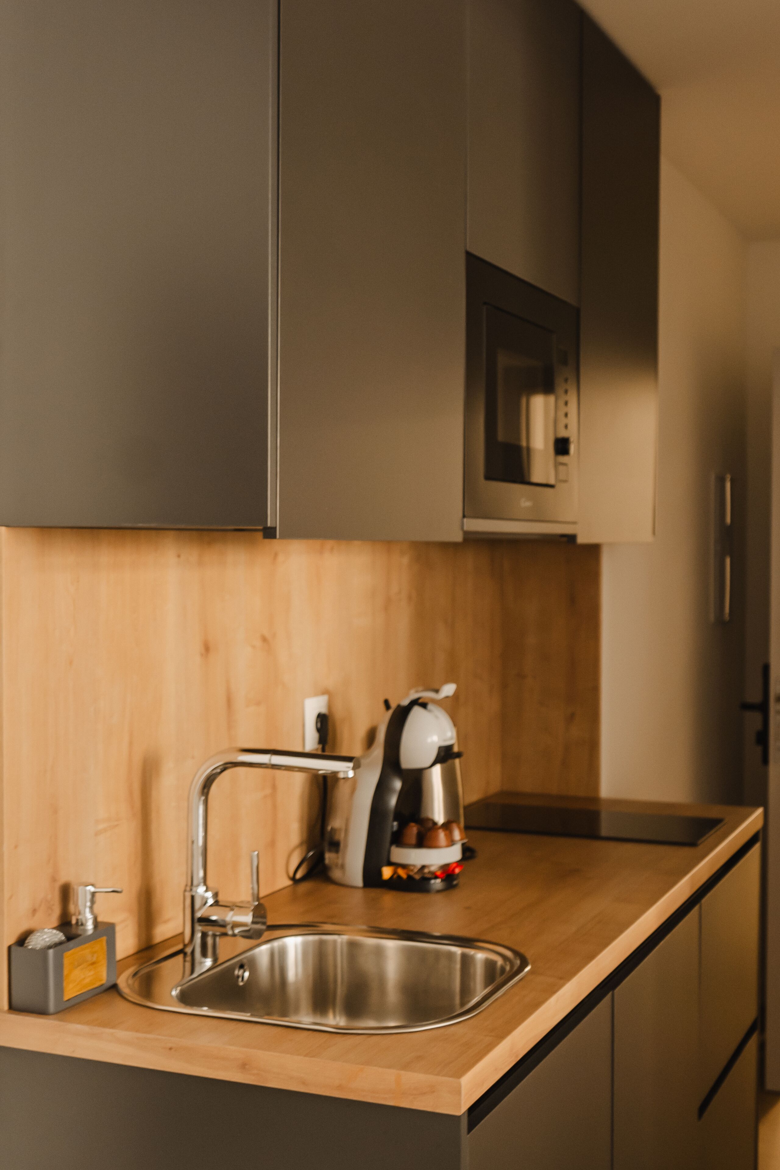 A modern kitchen with a stainless steel sink, wooden countertop, and a built-in microwave.