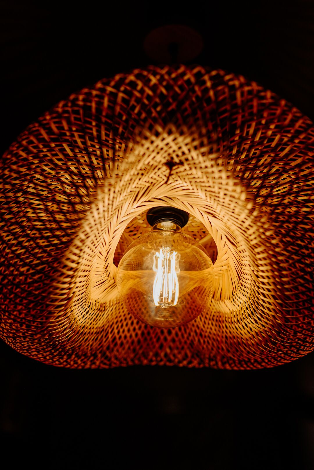Een detailopname van een geweven lamp met een gloeiende lamp in het midden.