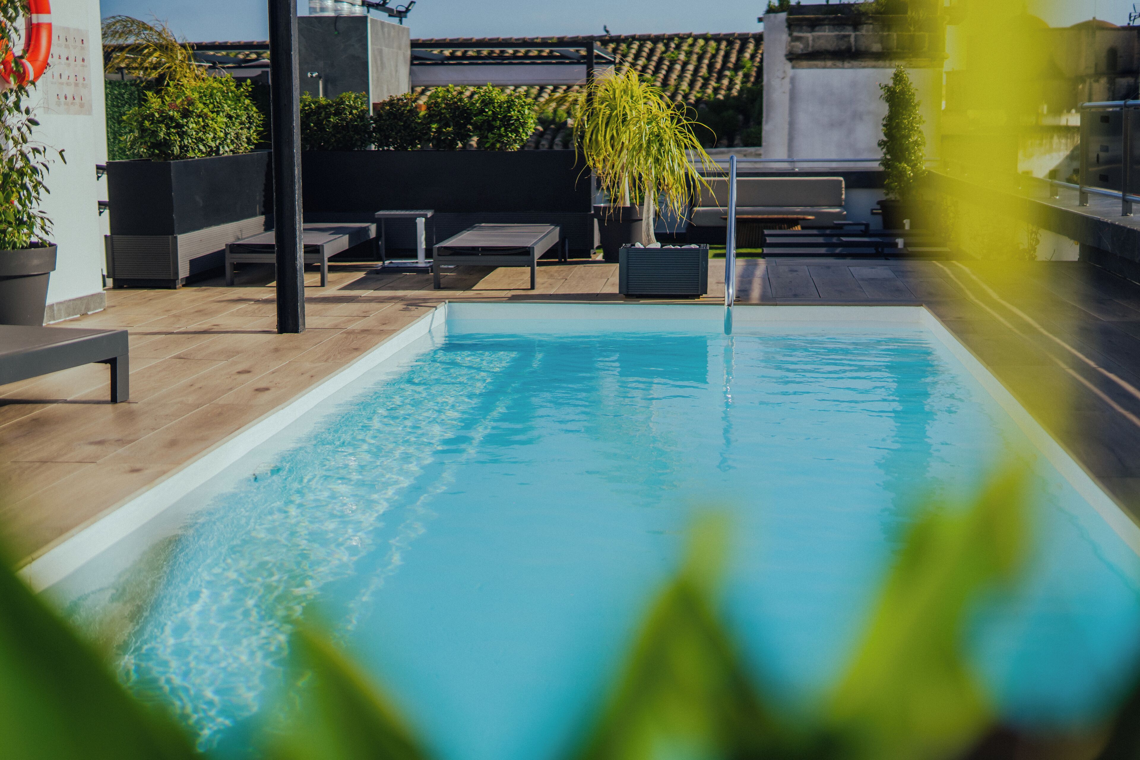 A rooftop pool with a clear blue water surface, surrounded by wooden decking and potted plants.