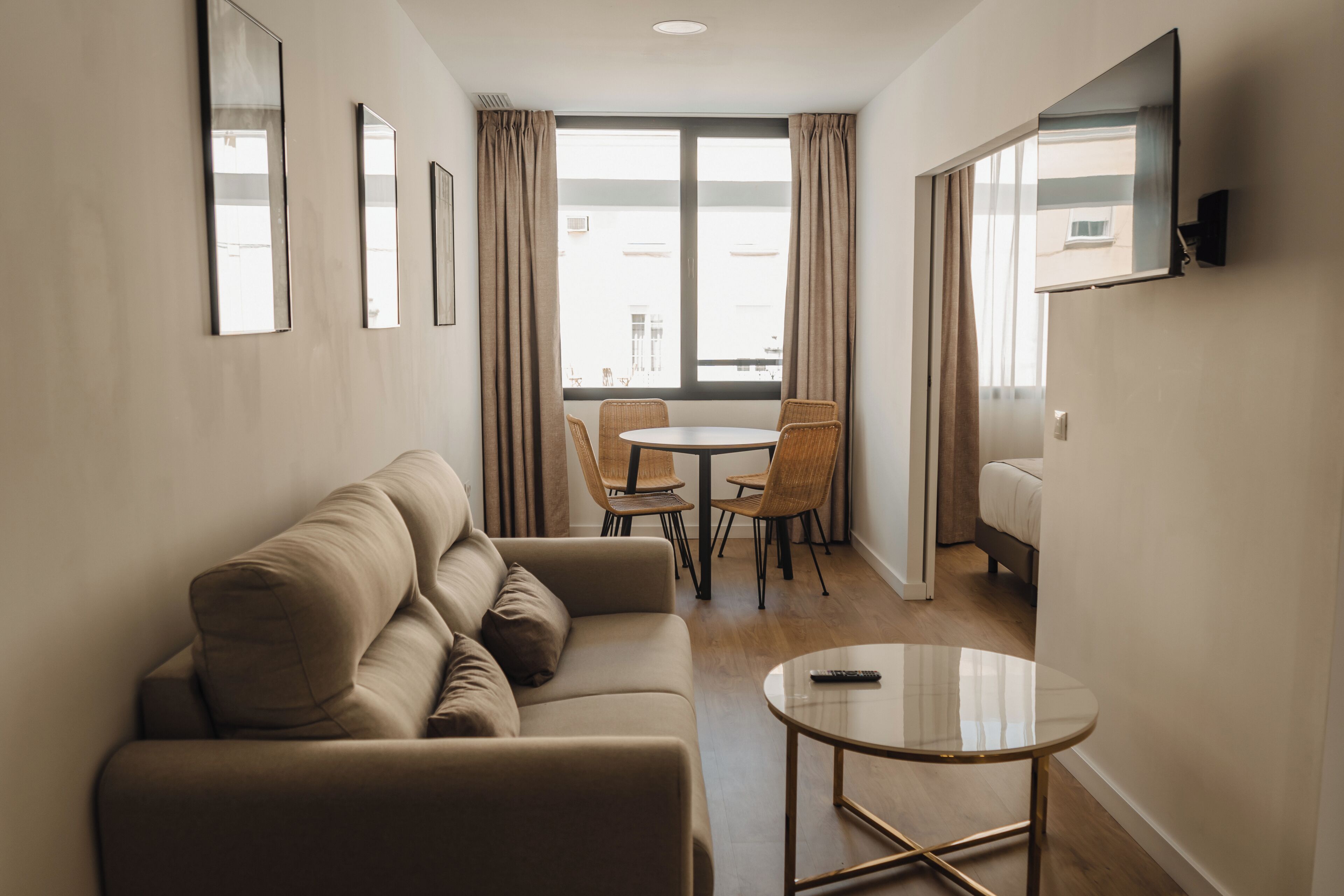 A modern hotel room with a sofa, a round table, and a TV mounted on the wall.