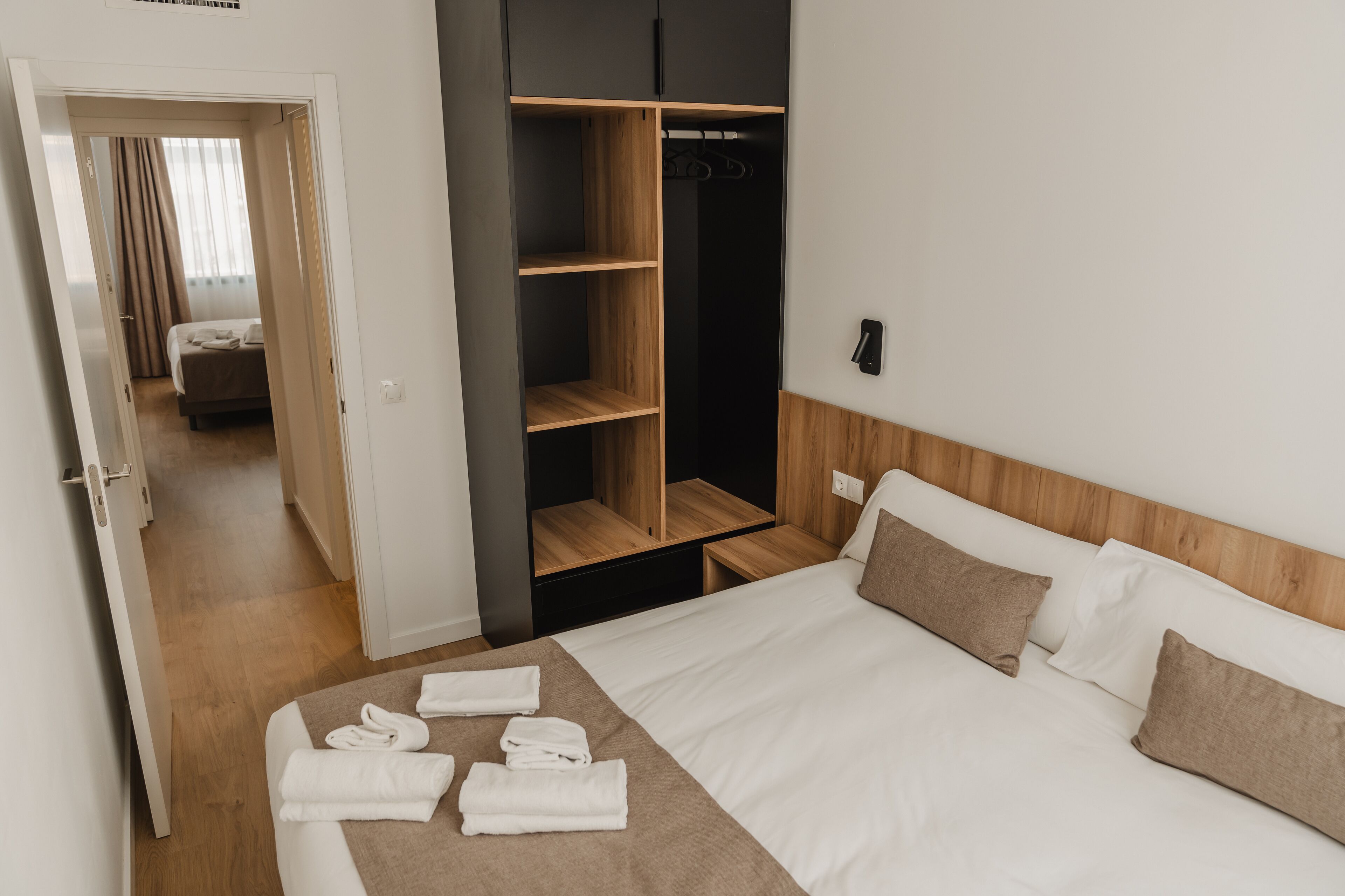 Een hotelkamer met een bed, een houten garderobe en een zichtbare badkamer door een geopende deur.