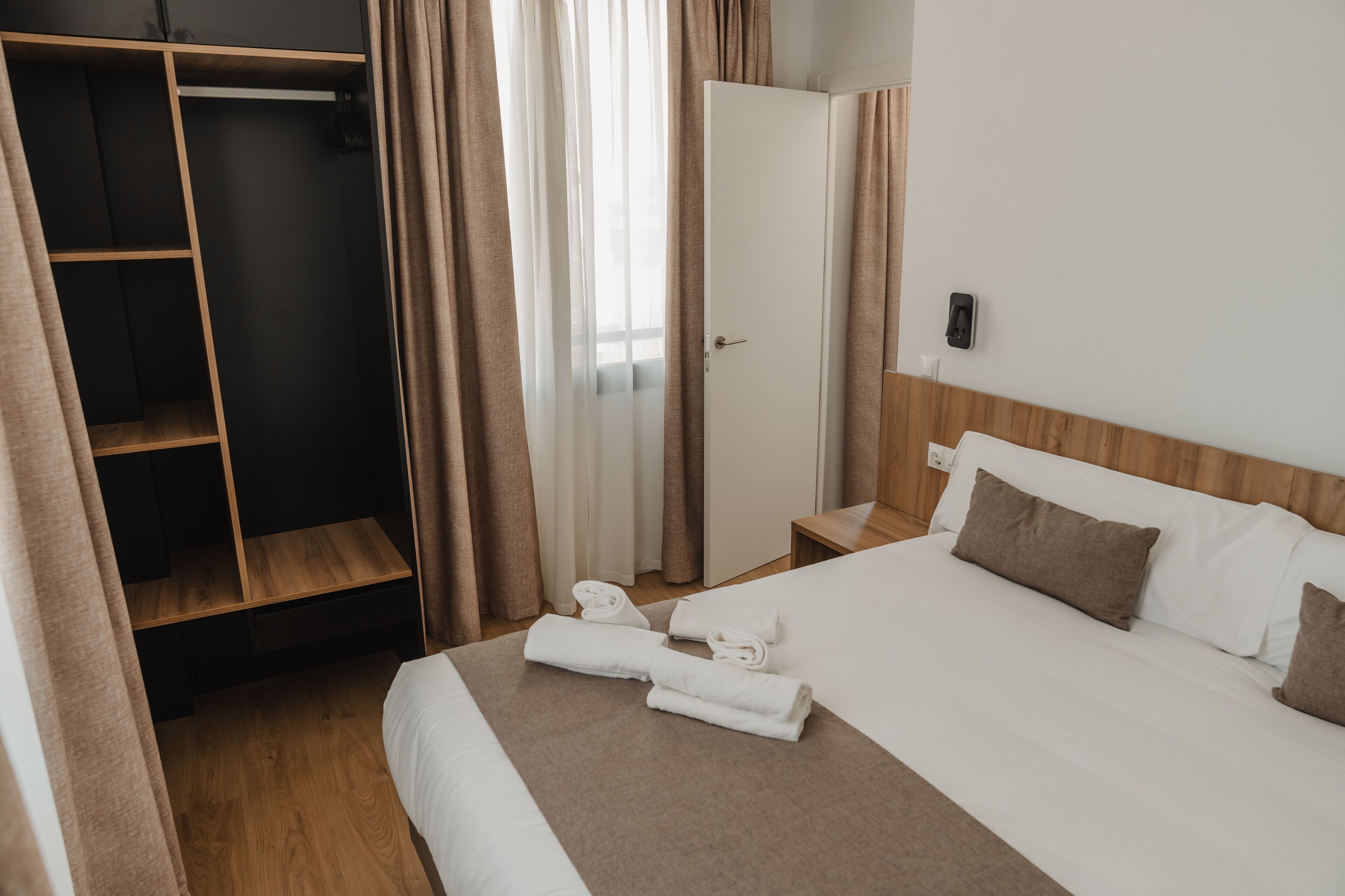 A hotel room with a bed, a wardrobe, a mirror, and a door.