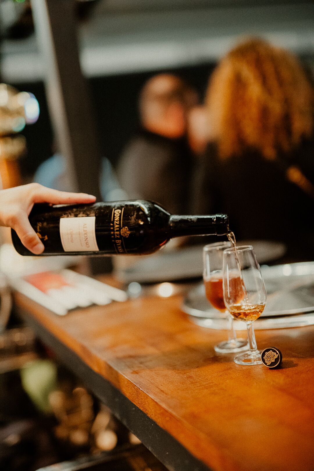 A hand pouring wine into a glass at a bar.