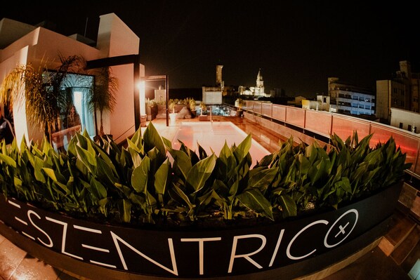 Una terraza en la azotea con un letrero que dice "ESENTRIC", rodeada de abundante vegetación.