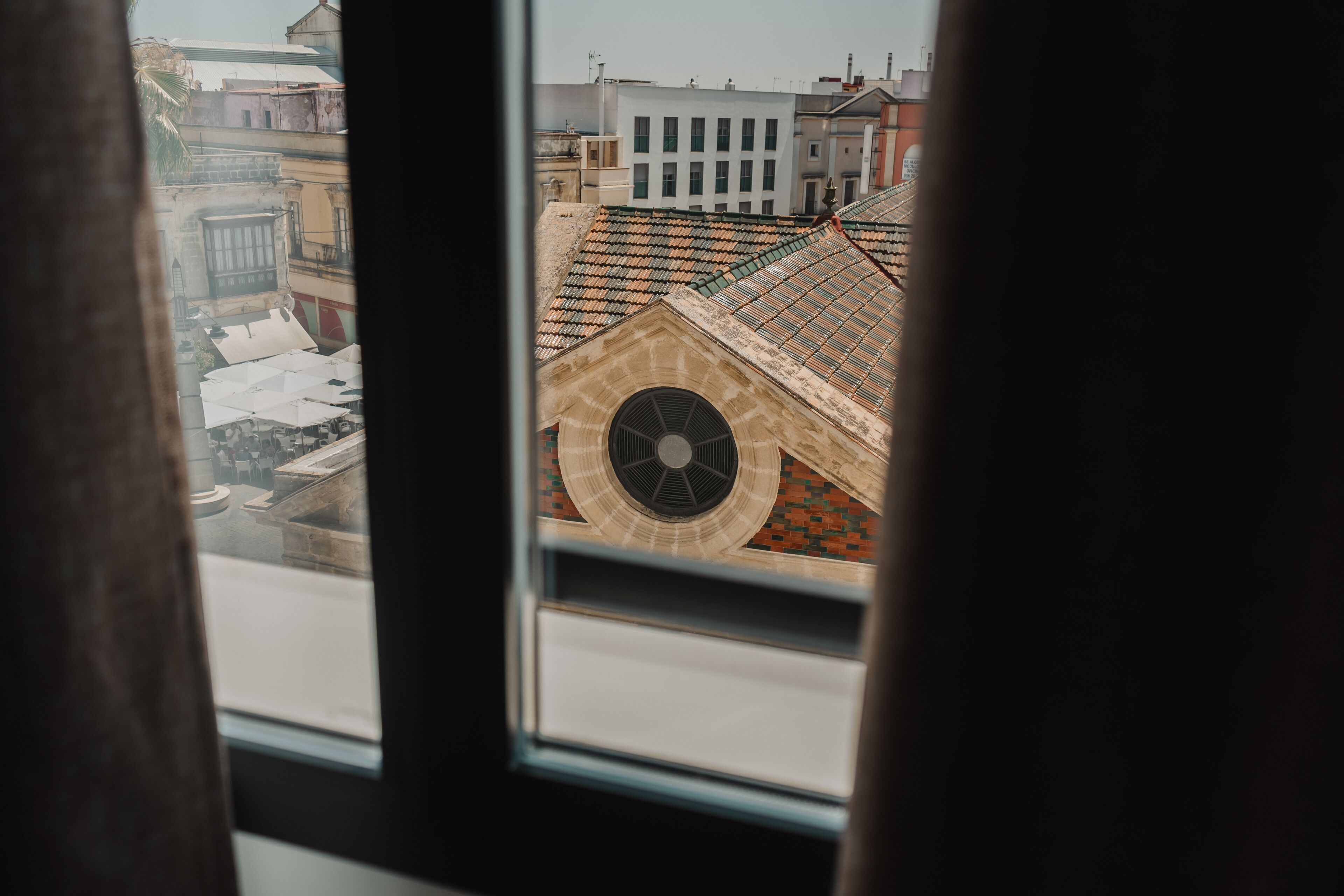 A view through a window of a building with a large circular window and a tiled roof.