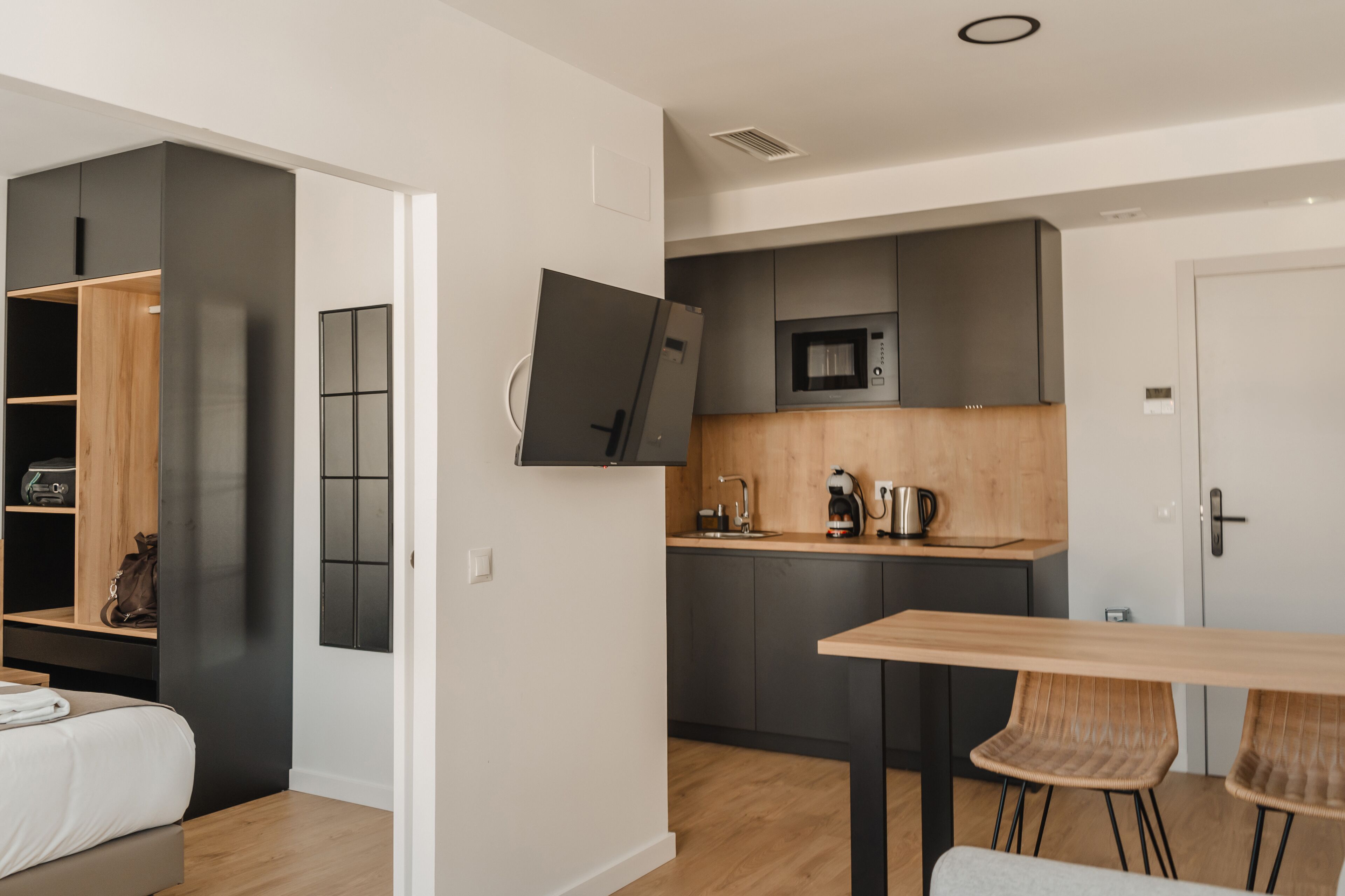 Una cocina moderna con microondas, cafetera y armarios de madera. Hay una mesa de comedor con dos sillas y una cama con cabecera de madera.