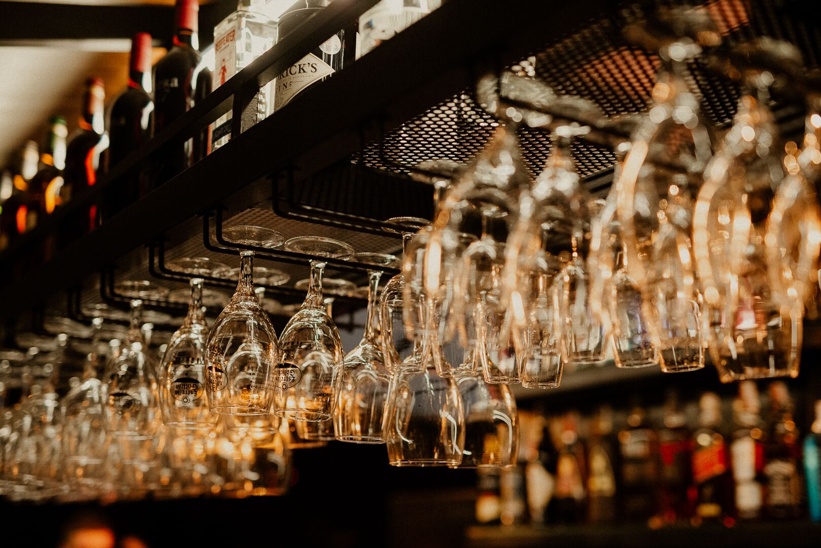 A bar with numerous empty wine glasses hanging from a rack, surrounded by shelves of various bottles.