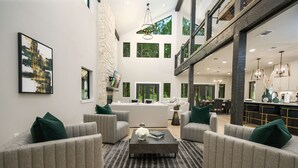 A spacious living area with a high ceiling, a central coffee table, and grey upholstered sofas with green cushions. - Custom Cabin w/ Games, Karaoke, Amazing Outdoor patio w/ swings - Sleeps 12 (Broken Bow)