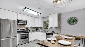 A modern kitchen with stainless steel appliances, white cabinets, and a wooden dining table with bar stools.