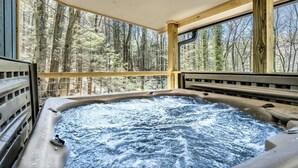 A hot tub with a view of a forest through large windows.