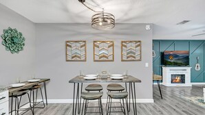 A modern kitchen with a dining table, bar stools, a chandelier, and a fireplace.