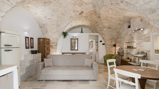 Ein gemütliches Interieur mit Steindecke, einer Couch, einem Esstisch mit Stühlen und einer Küchenzeile.