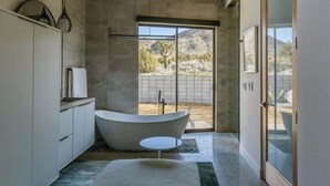 Ein modernes Badezimmer mit einer freistehenden Badewanne, einem Deckenventilator und einem großen Fenster mit Blick ins Freie.