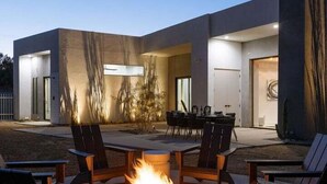 Eine Terrasse im Freien mit Feuerstelle, Sitzgelegenheiten und einem modernen Gebäude im Hintergrund.