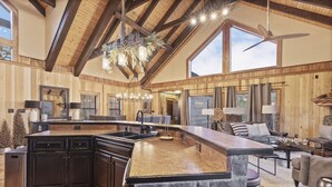 A spacious kitchen with a large island, wooden beams, and a ceiling fan. - Indigo Falls ~ 8BR w/Golf Simulator, Indoor Cave Pool, Hot Tub, Game Room, Theater, & Views! (Sevierville)