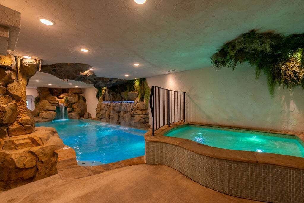 An indoor pool with a waterfall feature, surrounded by rock formations and a tiled floor.