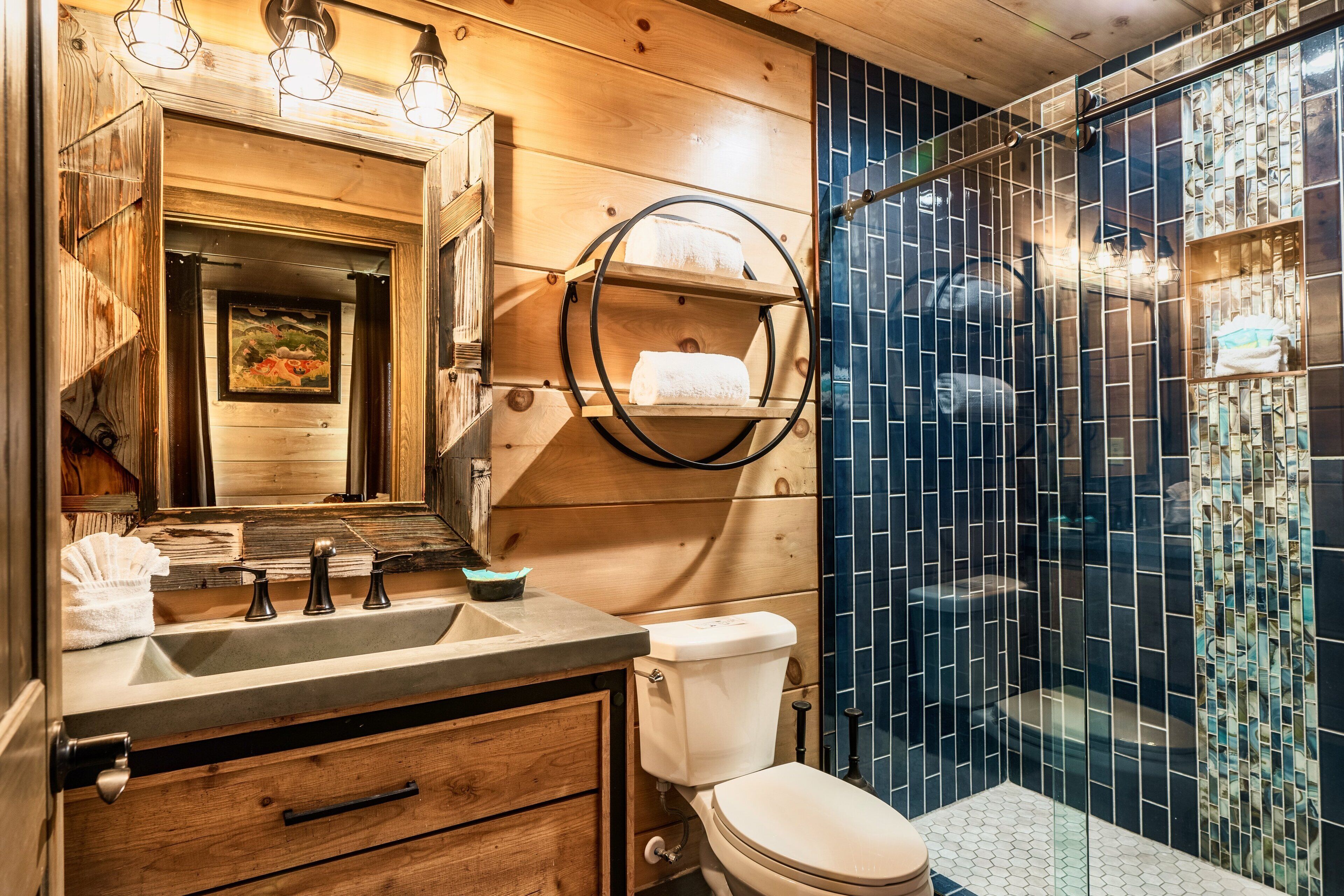 A bathroom with a wooden vanity, a toilet, and a shower area with blue mosaic tiles.