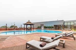 Uma piscina no terraço com espreguiçadeiras e um gazebo.