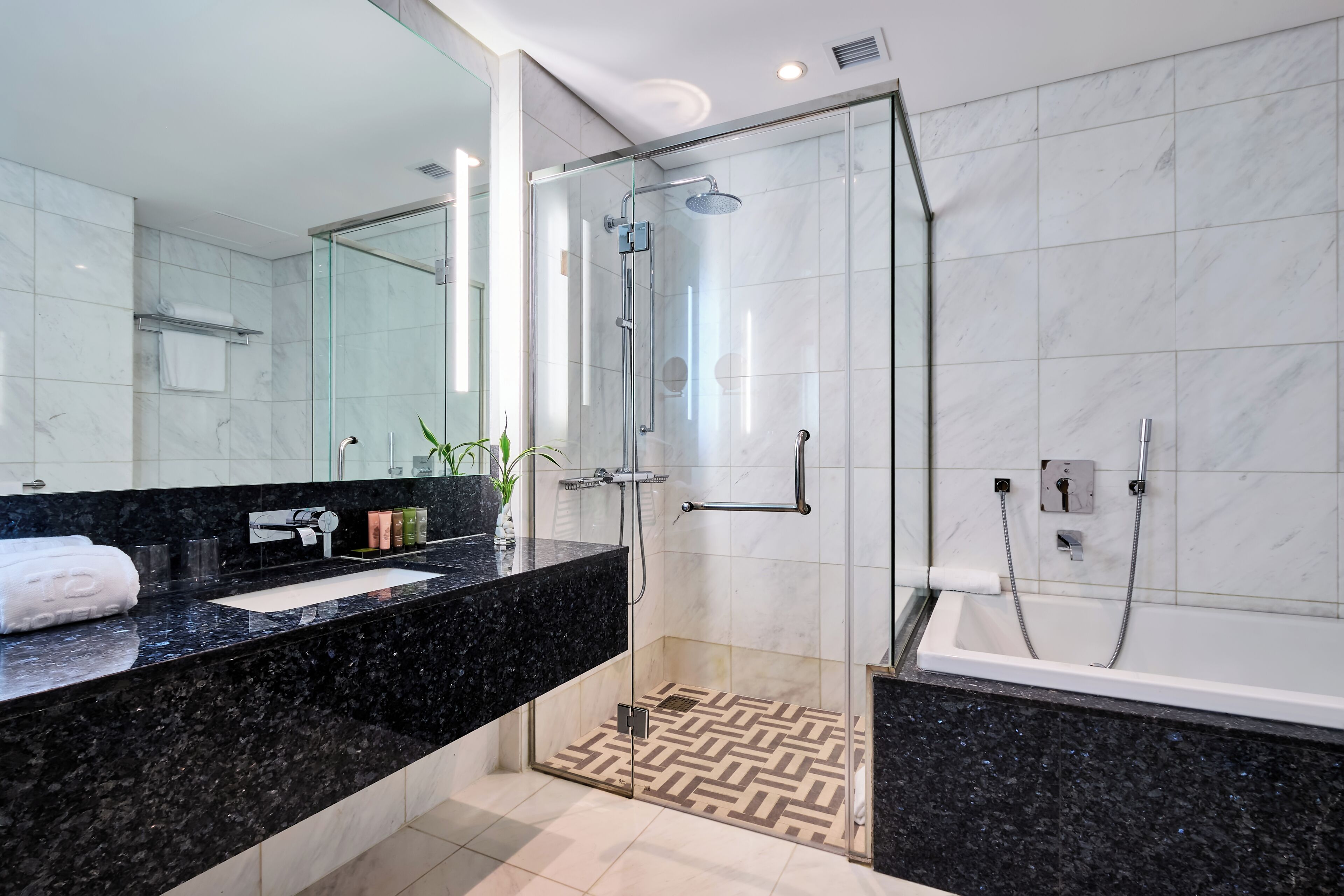 A modern bathroom with a glass-enclosed shower, a black marble sink, and a white tiled floor.