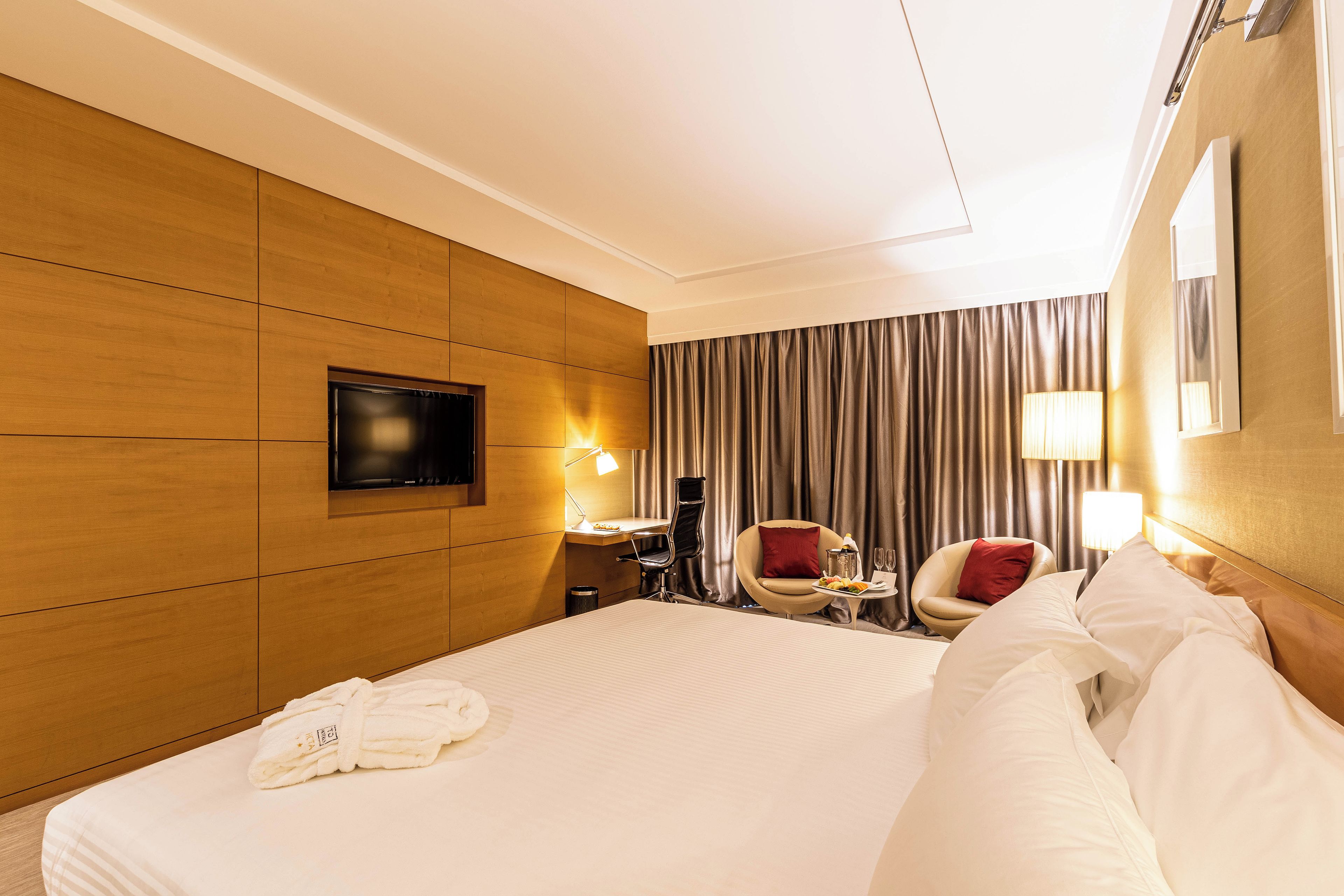 A hotel room with a large bed, a desk with a chair, a TV, and a window with curtains.