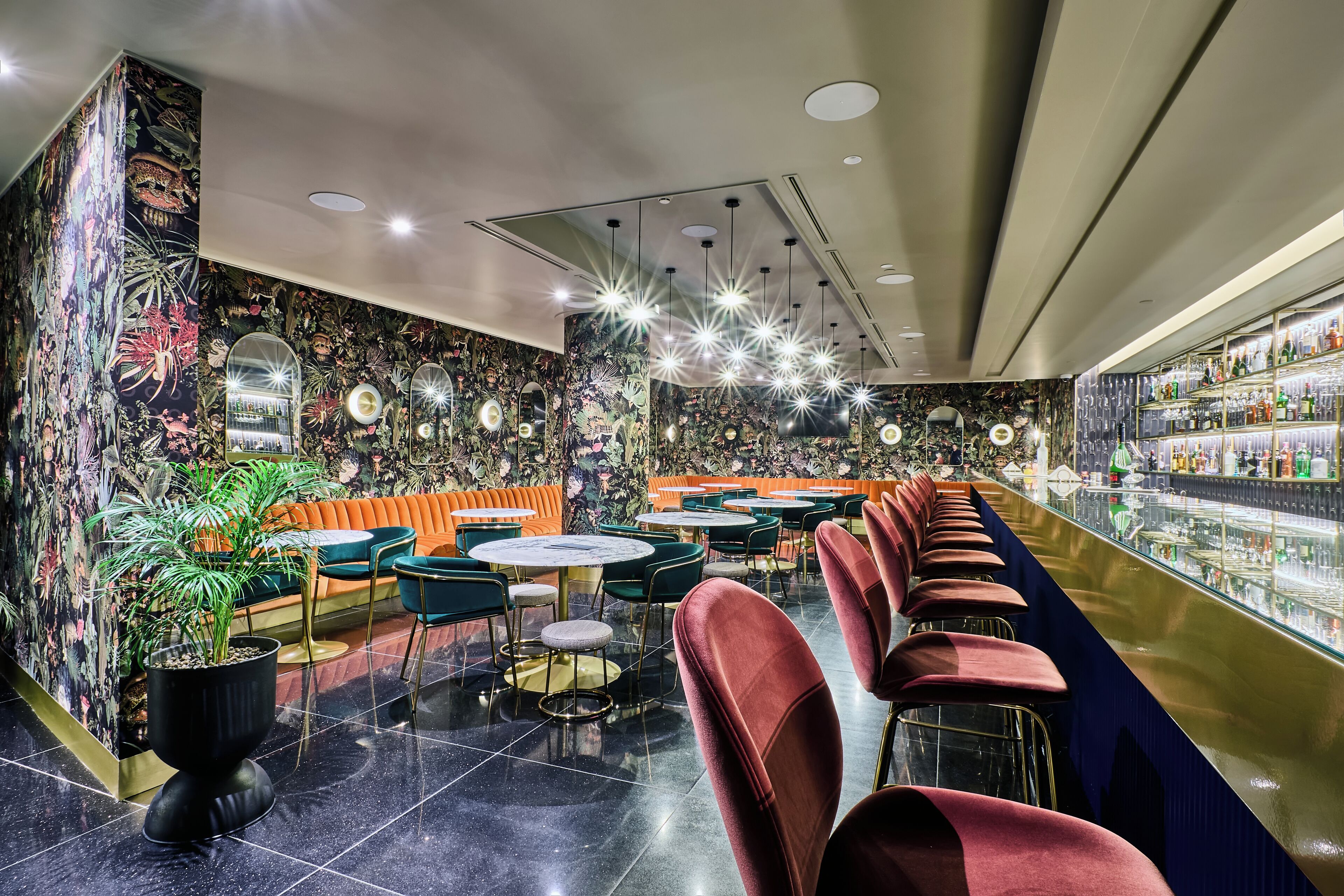 Un bar moderno con una barra larga, diversas opciones de asientos, incluyendo un sofá y sillas, y una pared decorativa con un mural floral.