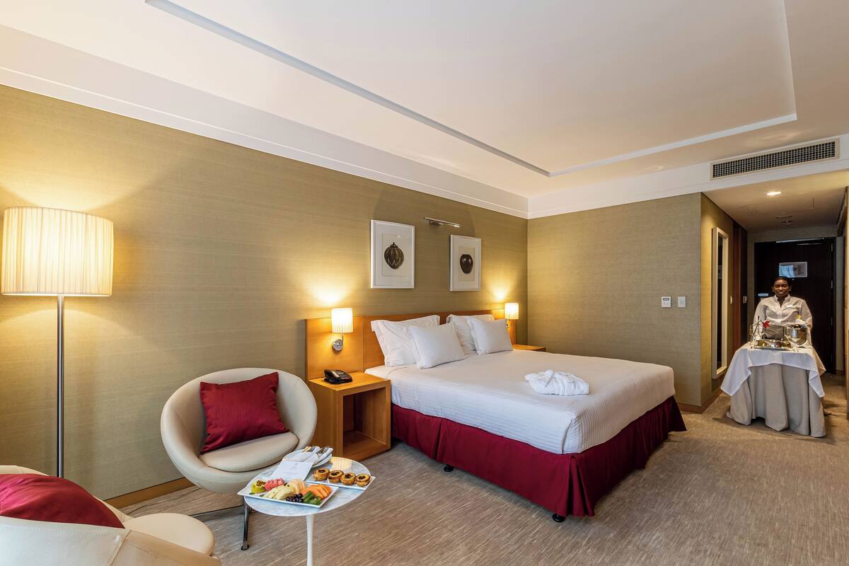 Une chambre d’hôtel avec un lit, une chaise, une table de chevet avec une lampe et une petite table avec des collations.
