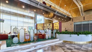 Eine geräumige Lobby mit Schachbrettmuster-Boden, einer zentralen Sitzecke mit Sofas und einem Couchtisch, sowie einer Präsentation verschiedener Gegenstände auf Regalen.