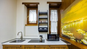 A kitchen with a double sink, a kettle, a microwave, and a shelf with dishes.