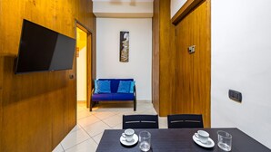 A modern room with a wooden wall, a flat-screen TV, a blue sofa, and a dining table with chairs.
