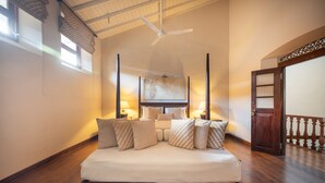 Ruime slaapkamer met een groot bed, houten vloer, plafondventilator en uitzicht op het balkon.
