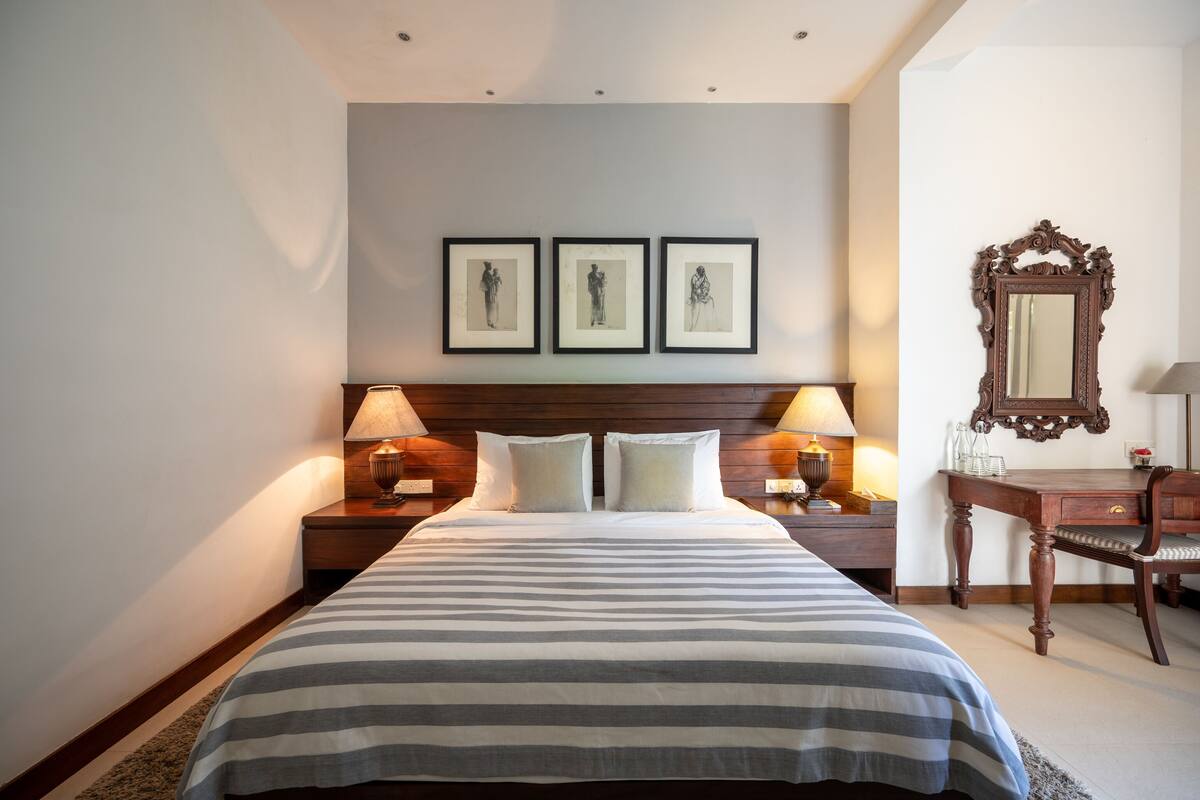 A hotel room with a large bed, two bedside tables with lamps, a wooden desk, and a mirror.