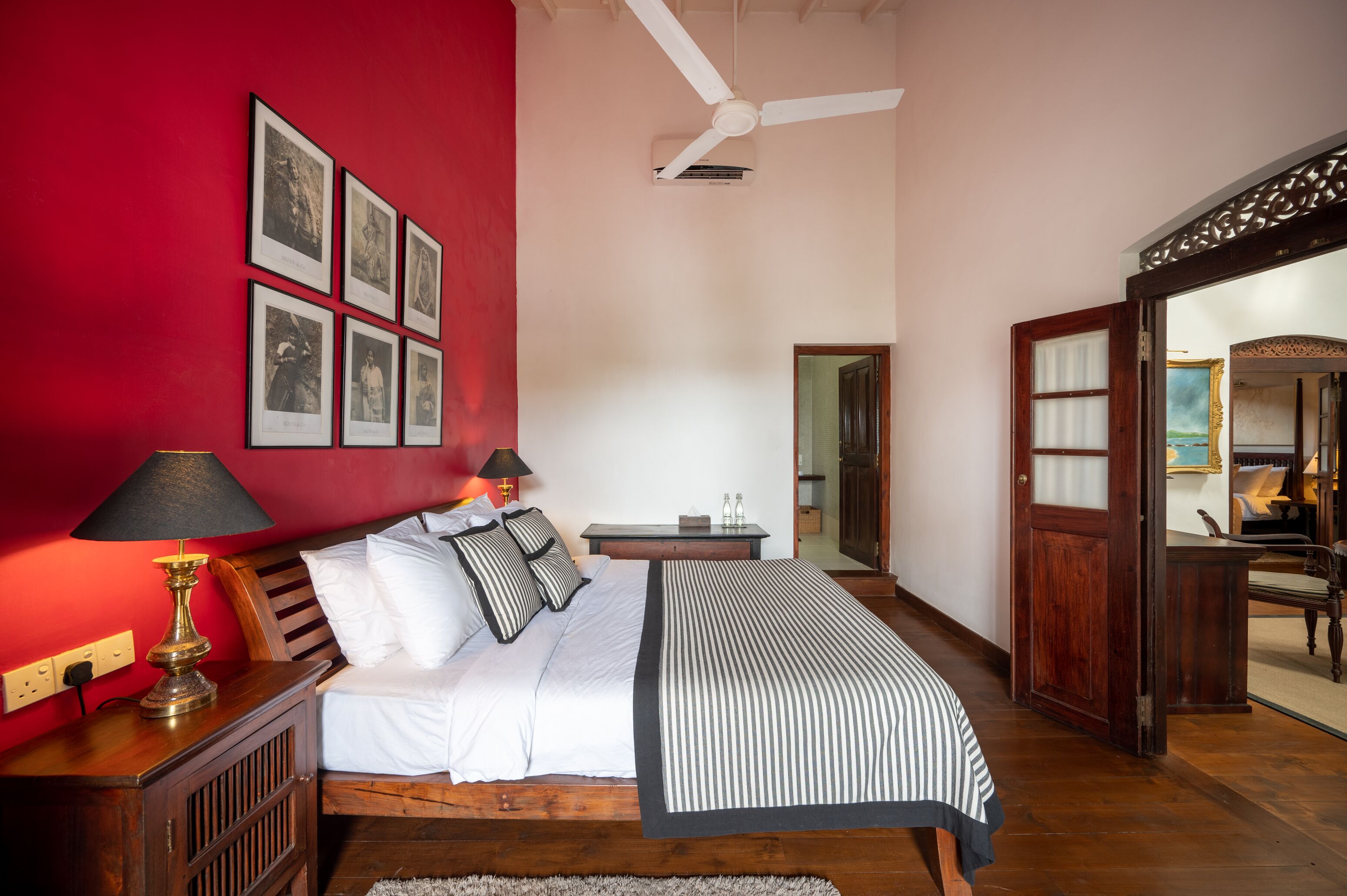 Une chambre à coucher comprenant un lit, une table de chevet, une lampe, un ventilateur de plafond et un miroir.