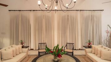 A spacious living room with a large chandelier, two sofas, a coffee table, and a view of the sky through the windows.