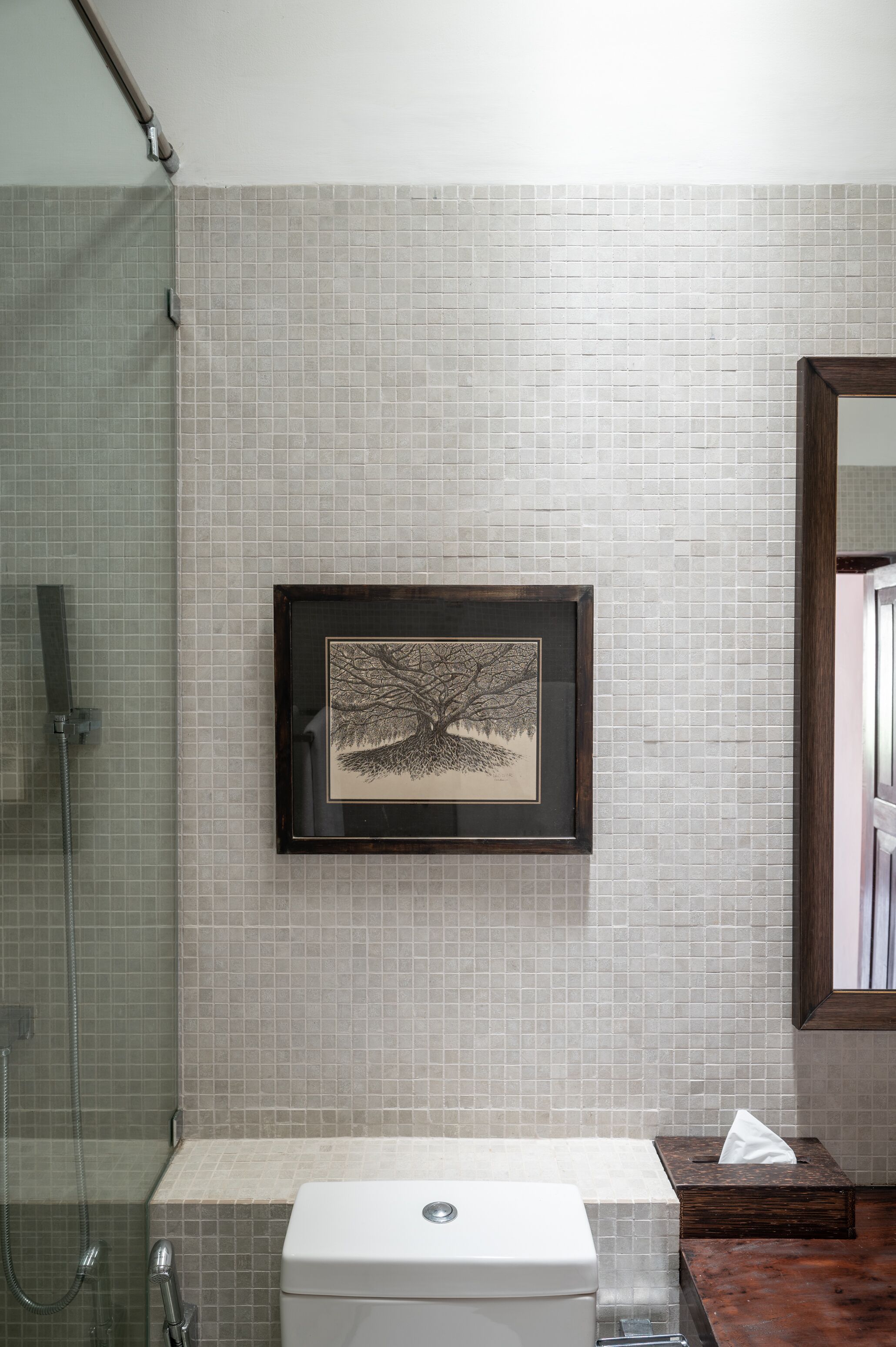 Une salle de bain avec un mur carrelé, un tableau encadré représentant un arbre, des toilettes et un espace douche.