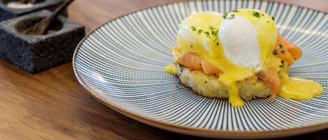A plate of eggs benedict with hollandaise sauce and poached eggs on a striped plate.