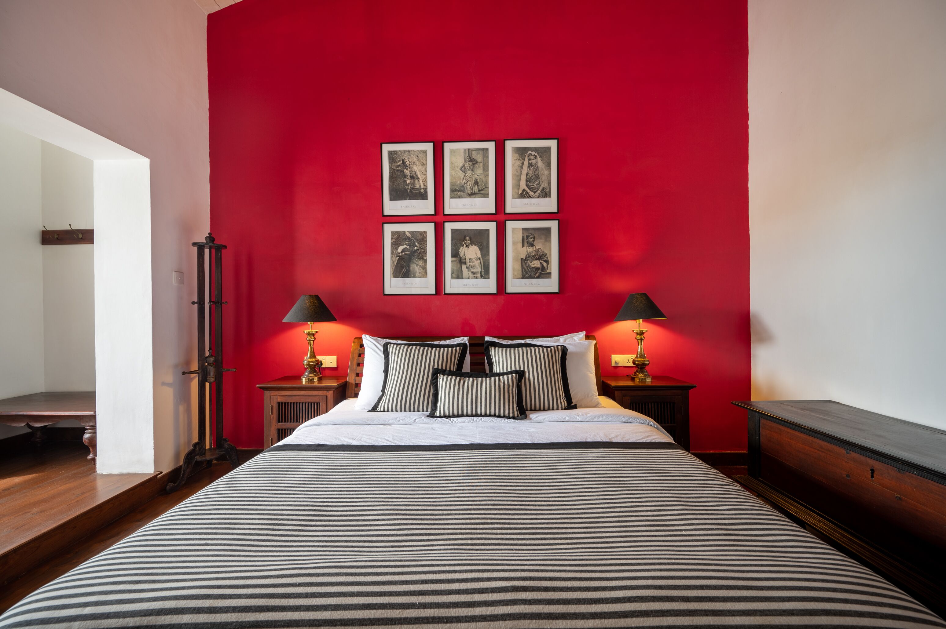 Une chambre d’hôtel avec un grand lit, un mur d’accent rouge et des tableaux encadrés au-dessus du lit.