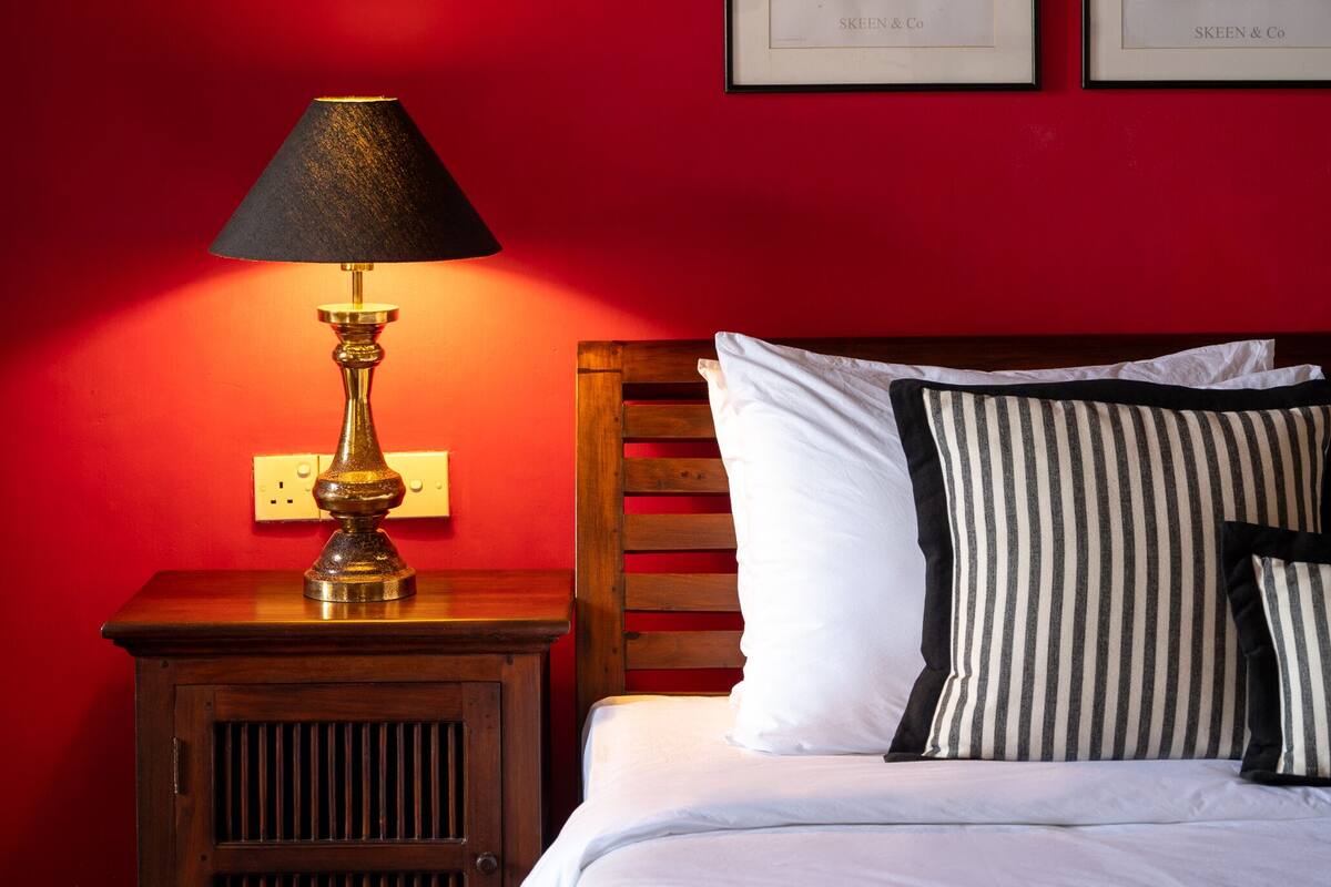 A room with a bed, a nightstand with a lamp, and four framed photographs on the wall.